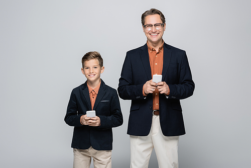 Smiling parent and son  while holding smartphones isolated on grey