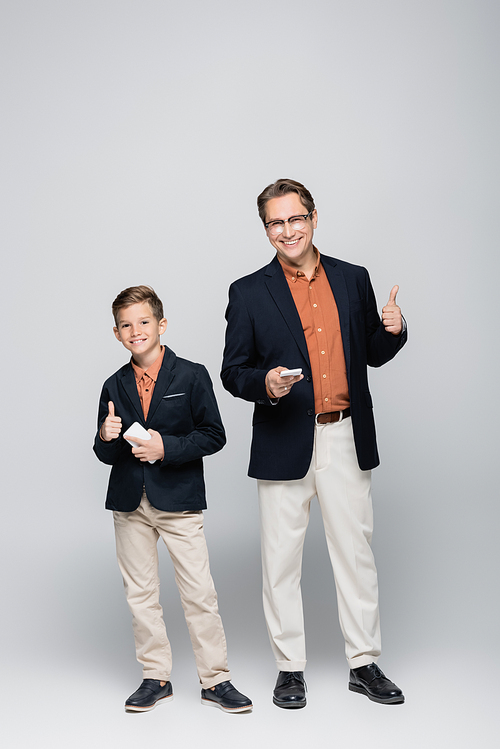 Smiling father and son holding smartphones and showing like on grey background