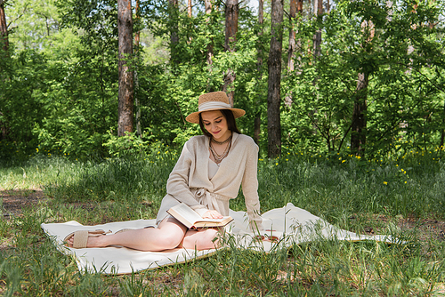 happy young woman in straw hat reading book in forest