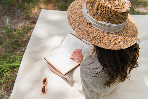overhead view of young woman in straw hat reading book in forest