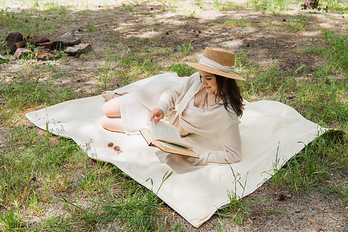 positive young woman in straw hat reading book in forest