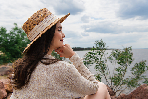 happy young woman in straw hat sitting near sea