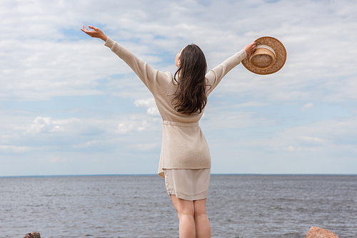back view of young woman standing with outstretched hands near sea