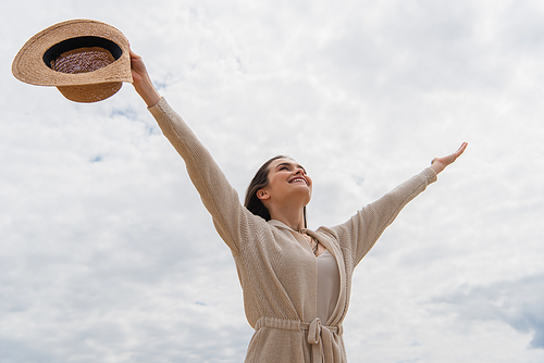 cheerful young woman standing with outstretched hands against cloudy sky