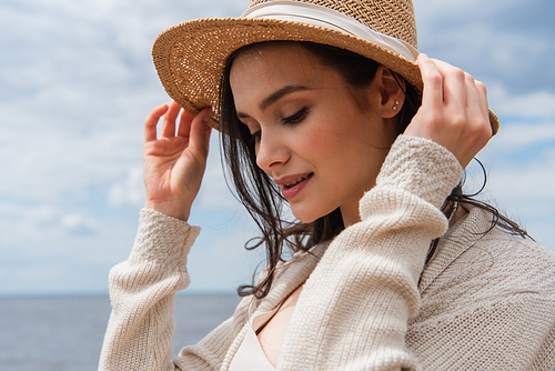 cheerful young woman adjusting sun hat outside