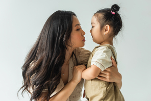 side view of stylish asian mother hugging toddler daughter isolated on grey