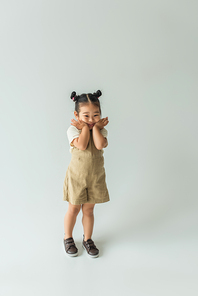 full length of happy asian toddler girl posing on grey