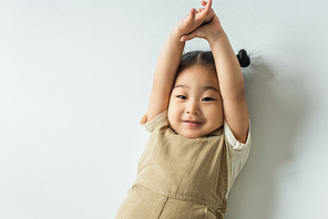 high angle view of cheerful asian toddler girl posing on grey