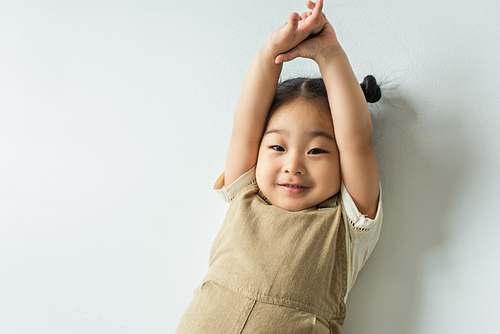 high angle view of cheerful asian toddler girl posing on grey