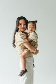 happy asian woman holding in arms toddler daughter isolated on grey