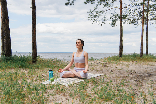 brunette woman in sportswear sitting in lotus pose and meditating on yoga mat