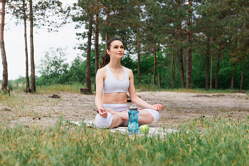 young woman in sportswear sitting in lotus pose and meditating on yoga mat