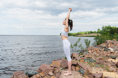 full length of young woman in sportswear practicing yoga near sea