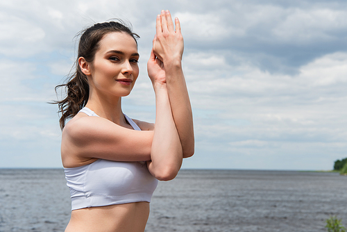 happy brunette woman practicing arms exercise near sea