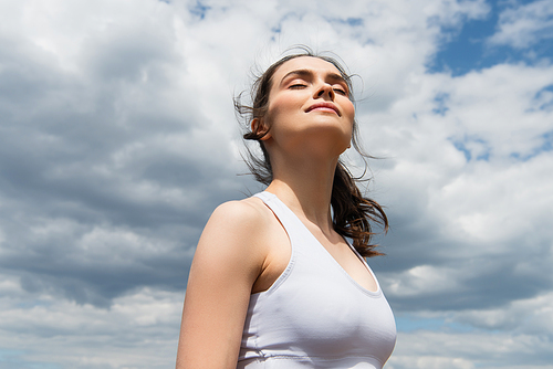 low angle view of young woman with closed eyes against blue sky with clouds