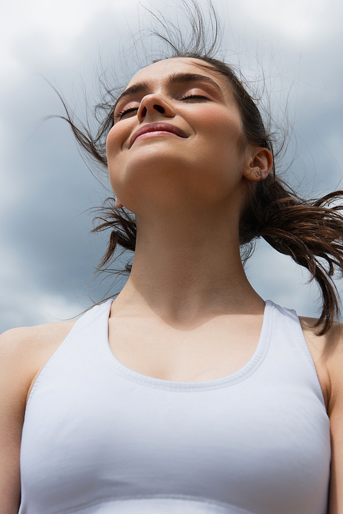 low angle view of young smiling woman in crop top against blue sky with clouds
