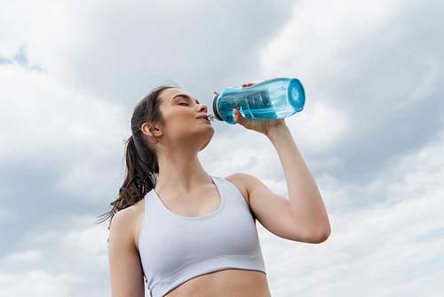 low angle view of brunette woman in crop top drinking water against  sky with clouds