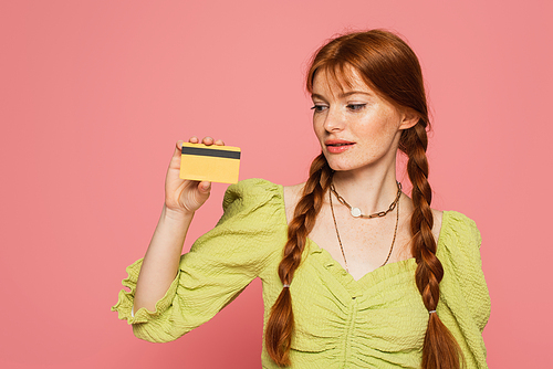 Freckled woman looking at credit card isolated on pink