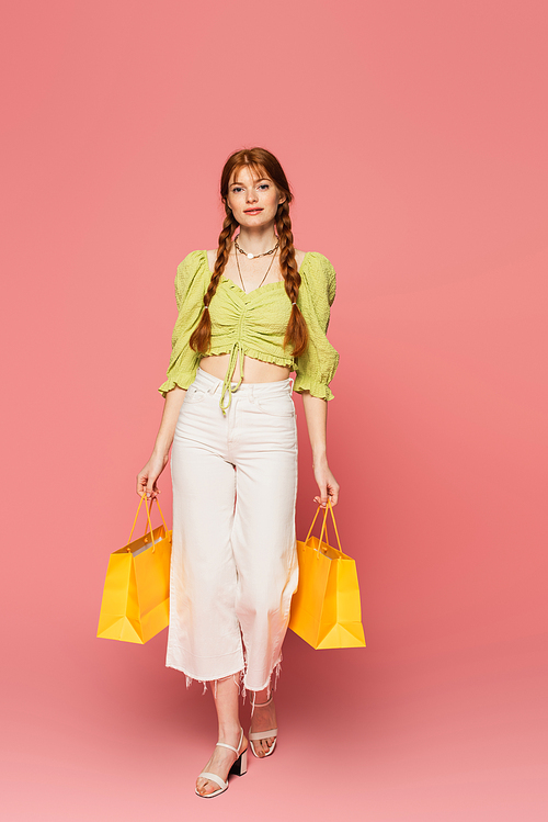 Pretty woman with freckles holding shopping bags on pink background