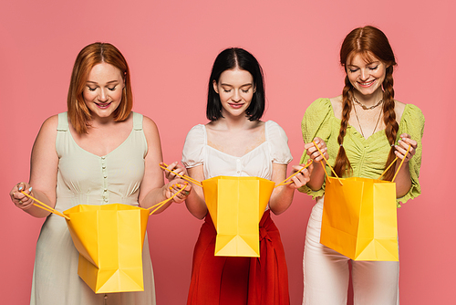 Body positive women looking at shopping bags isolated on pink