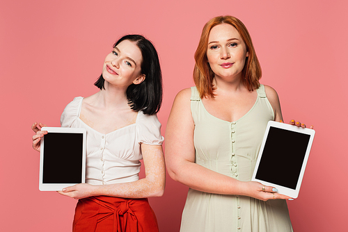 Body positive women holding digital tablets with blank screen on pink background