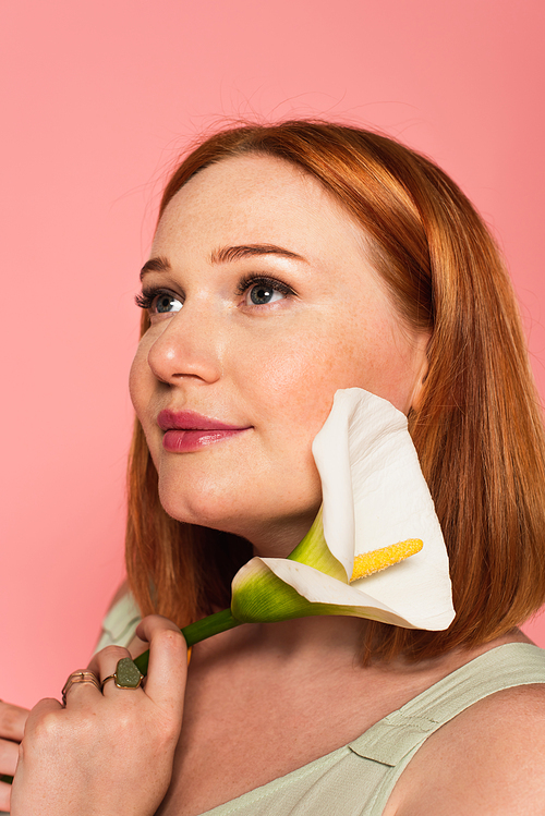 Pretty woman holding calla lily near face isolated on pink