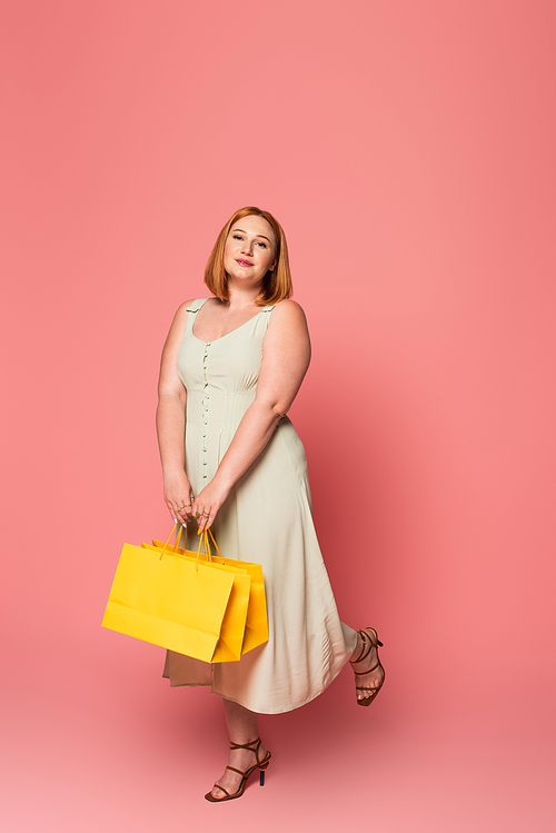 Fashionable plus size woman holding shopping bags on pink background