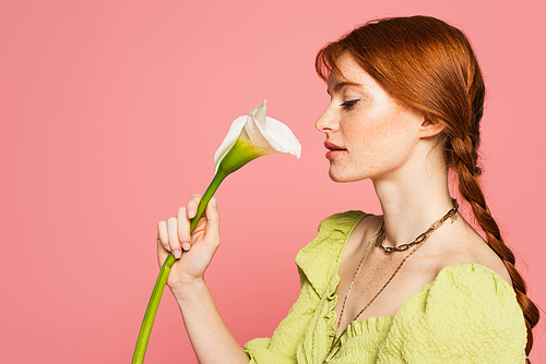 Side view of woman with freckles holding calla lily isolated on pink
