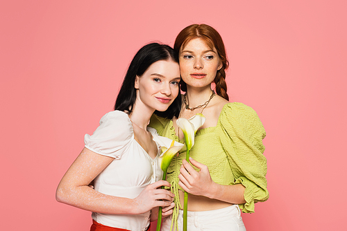 Women with freckles and vitiligo holding flowers isolated on pink