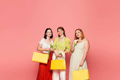 Smiling friends with shopping bags holding calla flowers isolated on pink
