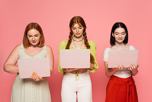 Pretty body positive women using laptops isolated on pink