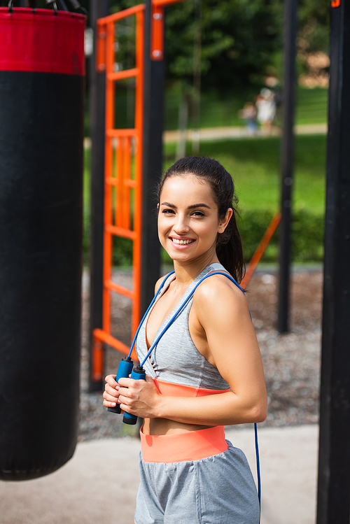 cheerful sportswoman holding jumping rope outside