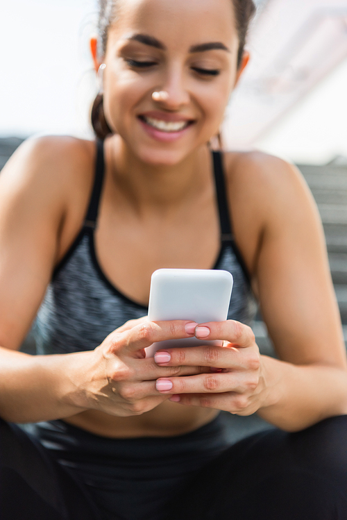 blurred and smiling sportswoman using smartphone outside