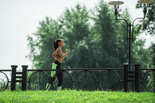 side view of happy and sportive woman in wireless earphones listening music while running in park