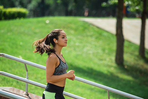 side view of sportswoman in wireless earphones listening music while running in park
