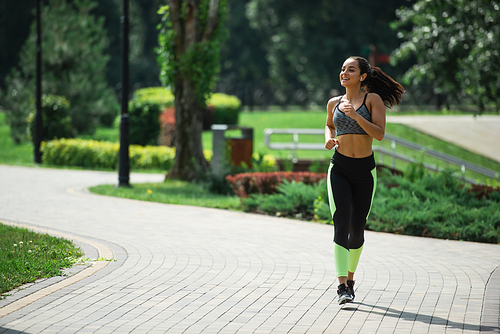 full length of smiling sportswoman in wireless earphones listening music while running in park