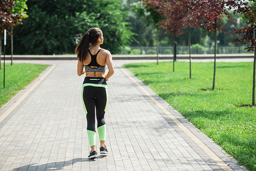 back view of sportive woman in wireless earphones listening music while running in park