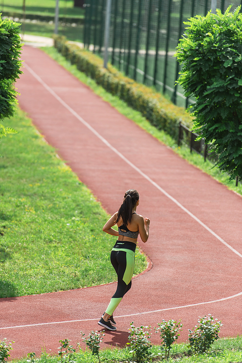 full length of sportive woman in crop top and leggings running on stadium
