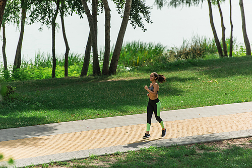 full length of happy sportswoman in wireless earphones listening music while running in green park
