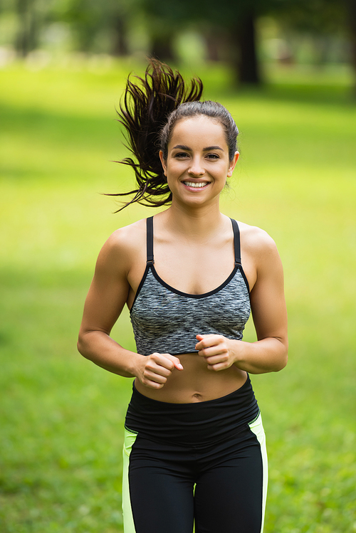 pleased young woman in crop top and leggings jogging in park