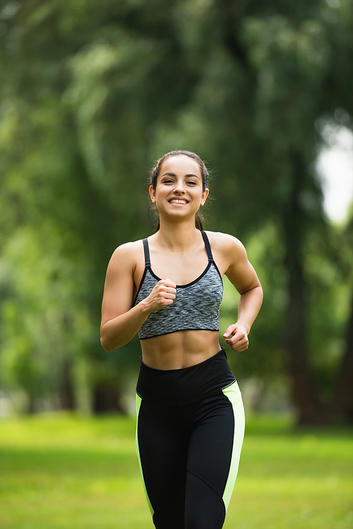 joyful young woman in crop top and leggings jogging in park