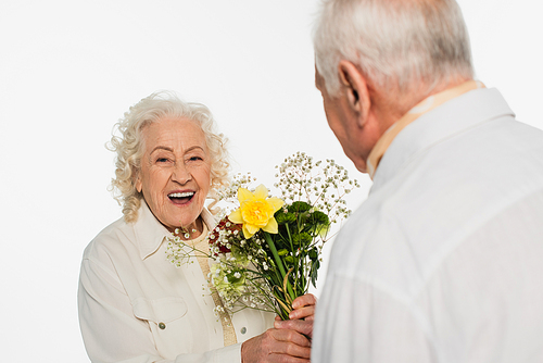 smiling elderly woman holding bouquet of flowers near blurred husband isolated on white