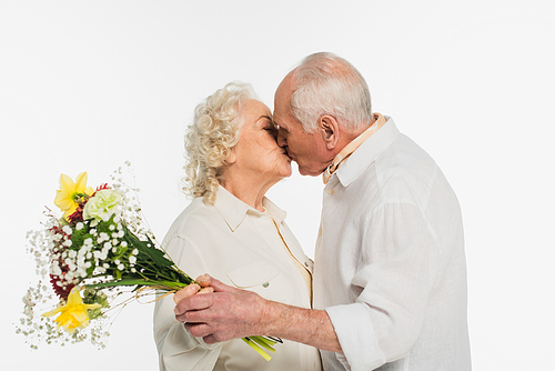 smiling elderly couple kissing and holding bouquet of flowers isolated on white