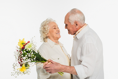 smiling elderly couple holding bouquet of flowers and looking at each other isolated on white