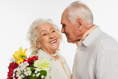 happy elderly man looking at smiling wife with bouquet of flowers isolated on white