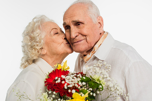 happy elderly woman holding bouquet of flowers and kissing husband isolated on white