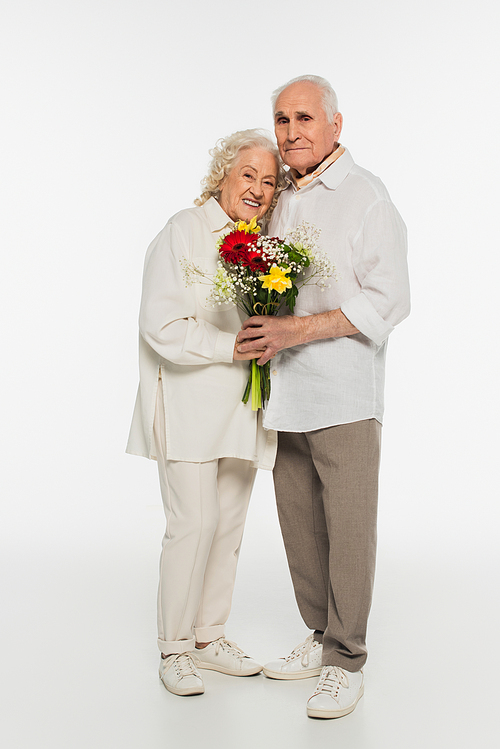 happy elderly couple hugging, holding bouquet of flowers and  on white
