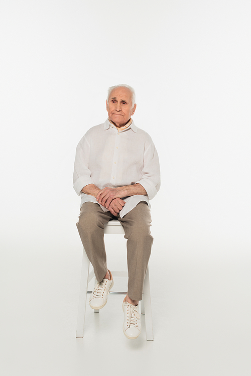 sad elderly man in casual clothes sitting on stool on white