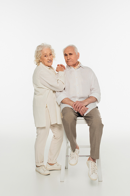 smiling elderly woman hugging husband sitting on stool on white