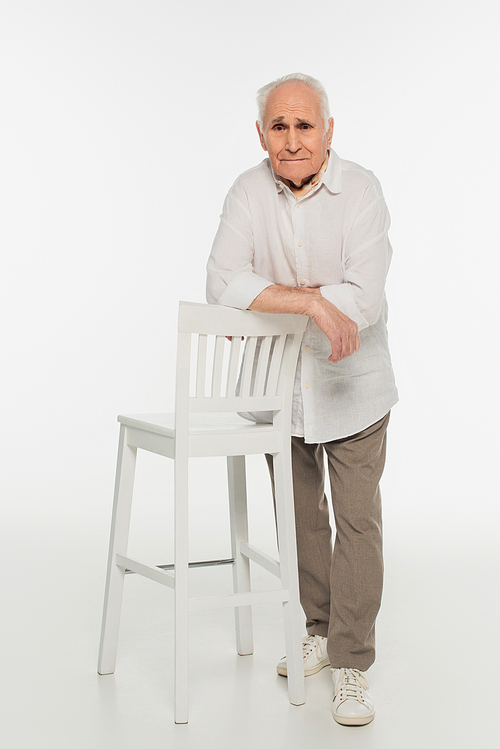 upset elderly man in casual clothes standing near stool and  on white